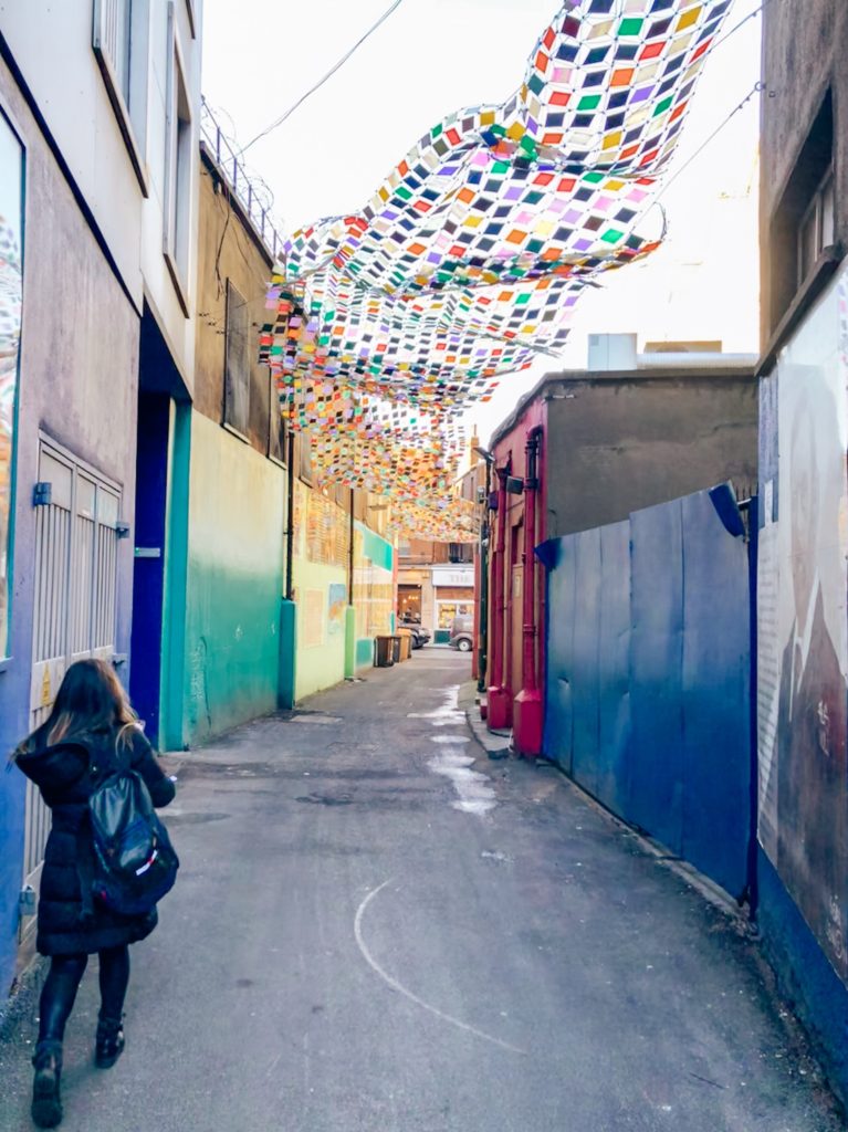 girl walking down alley in Dublin under mosaic art piece and bright colored walls
