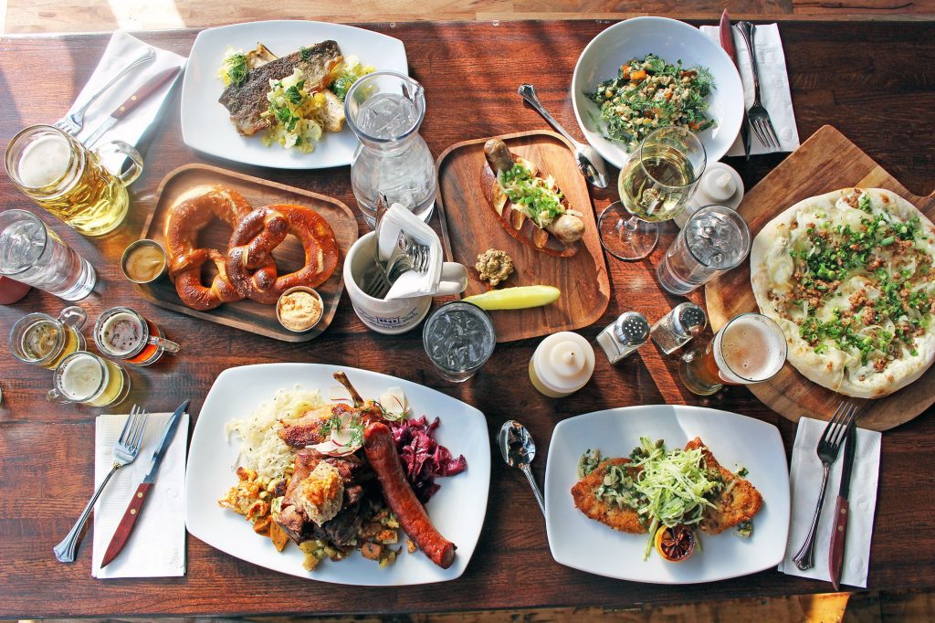 German Smörgåsbord of food from Rhein Haus restaurant featuring pretzels, Weiner schnitzels, gourmet brats, beers, salads, flatbreads