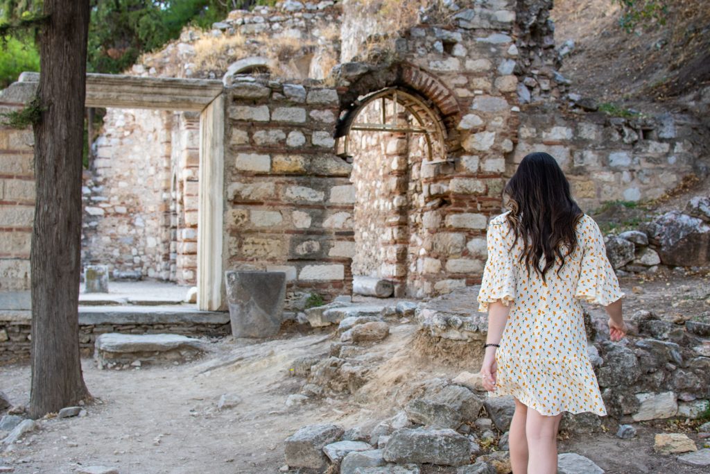 girl with long brown hair in a pretty dress exploring the old Church of St. Nikolaos inside the Acropolis