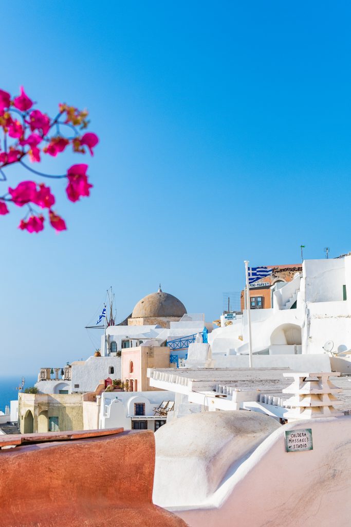 oia, santorini greece with pink bougainvilleas and white washed building, greek flags and domes in the background