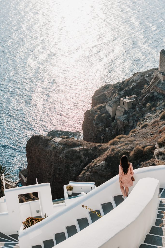 girl on white washed stairway in oia, santorini, greece overlooking the ocean and cliffside