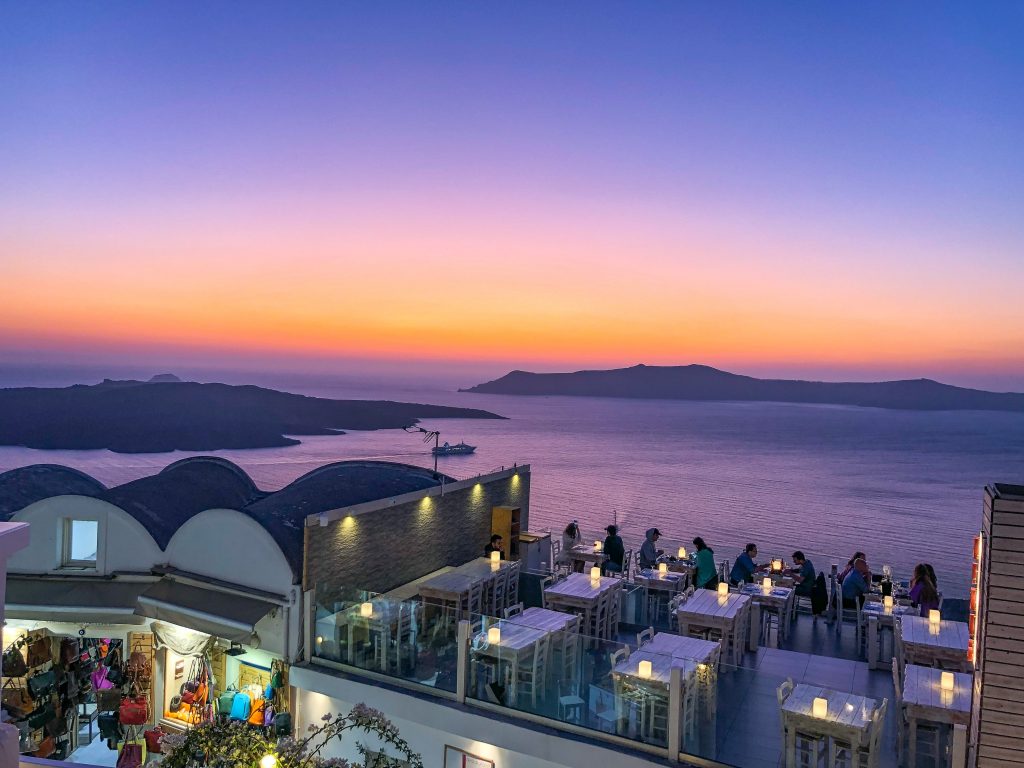 view of the sunset from argo restaurant in fira santorini with hues of purple gold orange yellow and blue colors setting over the caldera and aegean sea 