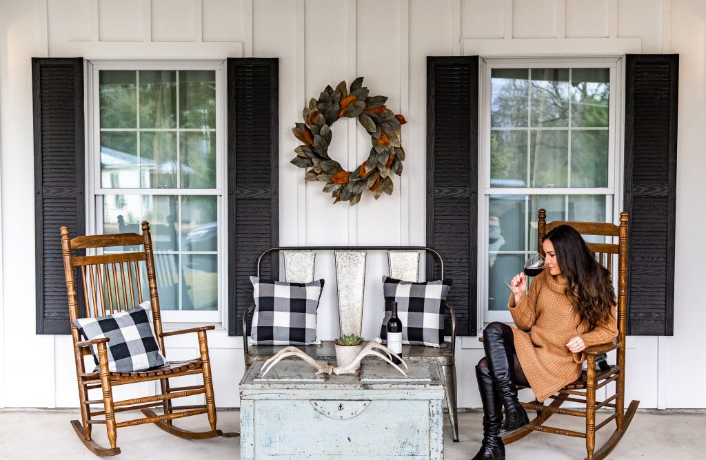 girl sitting on porch of emma haus fredericksburg airbnb rental drinking wine, airbnb rental fredericksburg texas, cute white cottage with large front porch in fredericksburg tx, charming texas hill country cottage rental