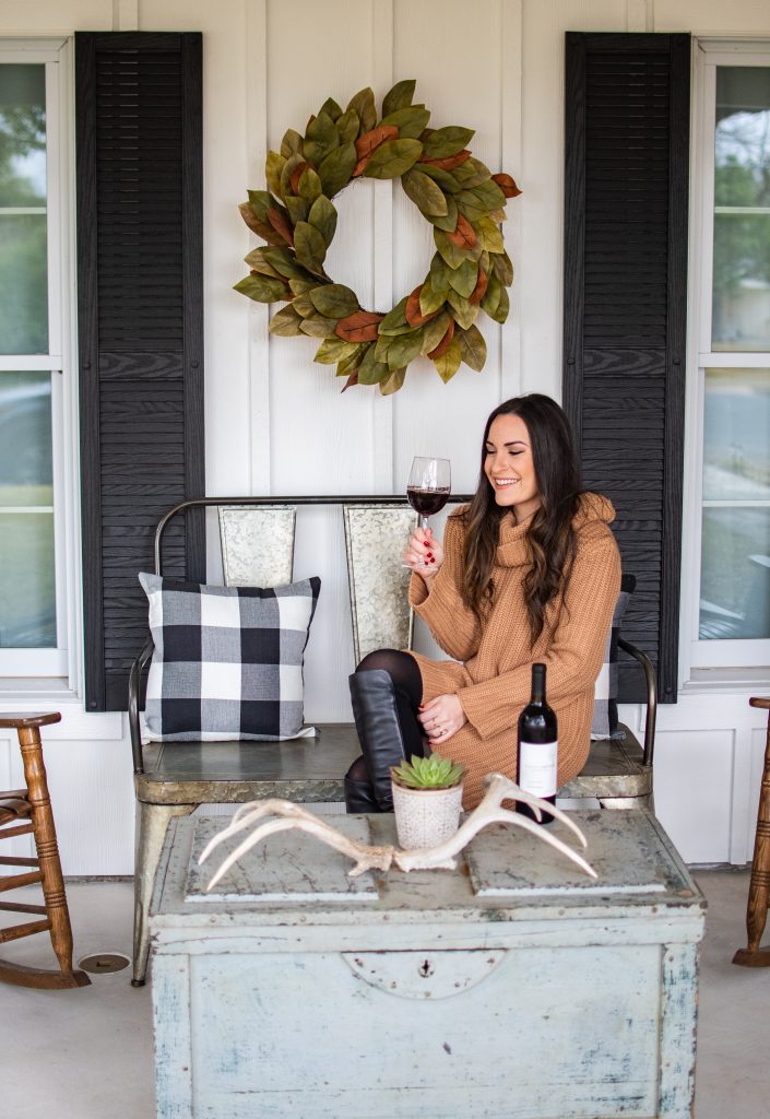 girl sitting on porch of emma haus fredericksburg airbnb rental drinking wine, airbnb rental fredericksburg texas, cute white cottage with large front porch in fredericksburg tx, charming texas hill country cottage rental