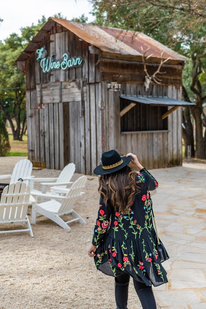 landry has landed, girl in black dress and black hat standing outside of the wine barn outdoors at signor vineyards in fredericksburg texas