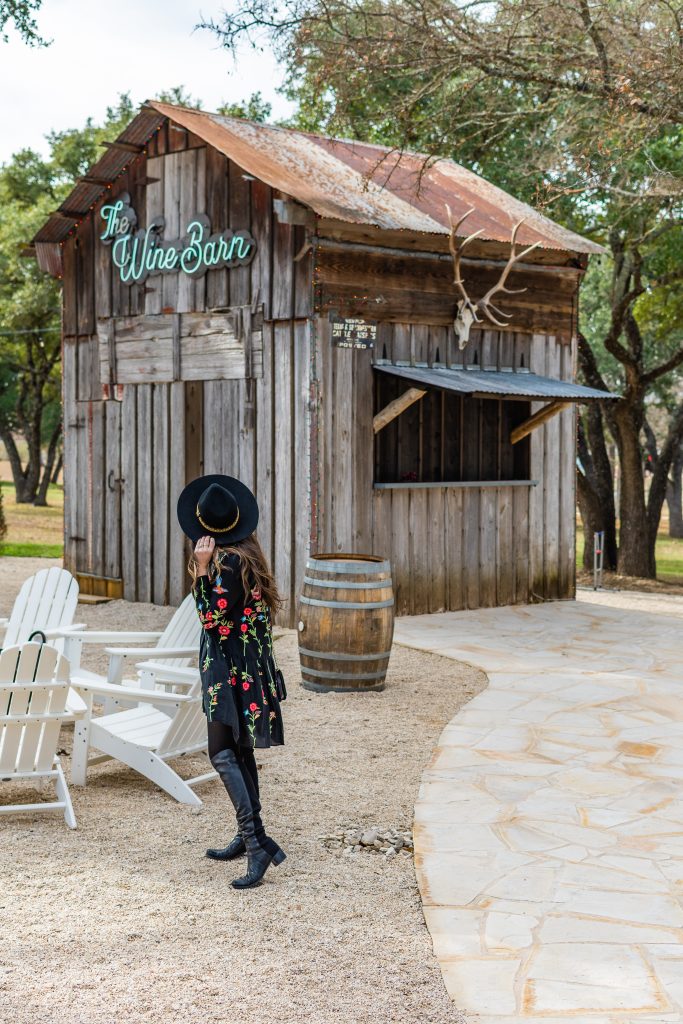 landry has landed, girl in black dress and black hat standing outside of the wine barn outdoors at signor vineyards in fredericksburg texas