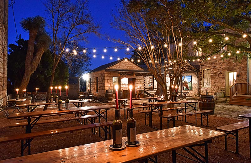 pontotoc vineyard weingarten in fredericksburg texas, pontotoc weingarten outdoor courtyard with string lights and picnic tables at dusk and wine bottle candles, best wineries in fredericksburg texas