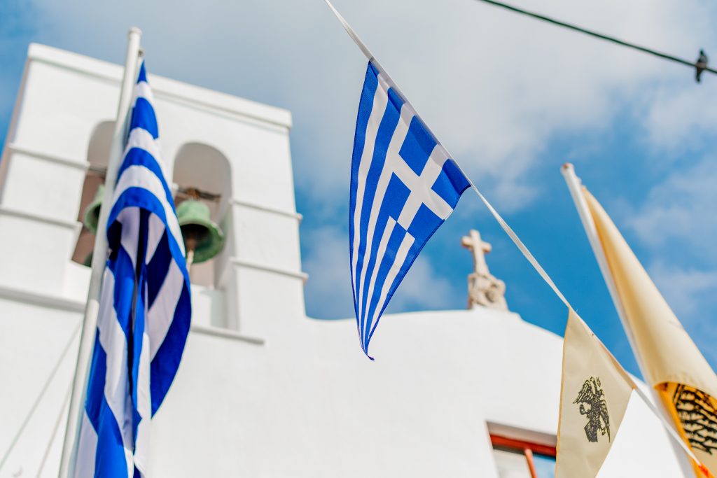 Greek and colorful flags hanging around Church of Panachrantos (Panachra), panachra church in mykonos, greece