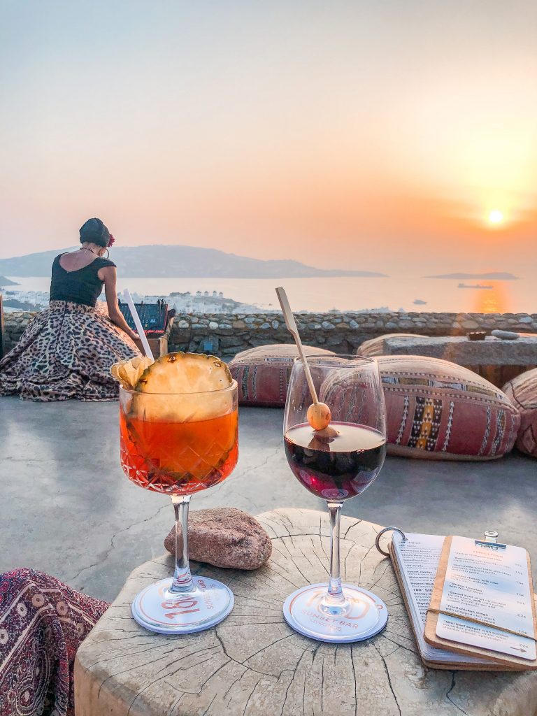 drinks and sunset view from 180° Sunset Bar in Mykonos Greece overlooking Mykonos Town and the windmills. Where to watch the sunset in mykonos, the best things to do in mykonos greece