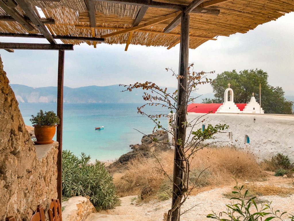 kiki's tavern mykonos, kiki's tavern restaurant agios sostis beach, best restaurants in mykonos, best things to do in mykonos, local cuisine mykonos, view of beach shack looking over agios sostis beach with church with red roof on the beach