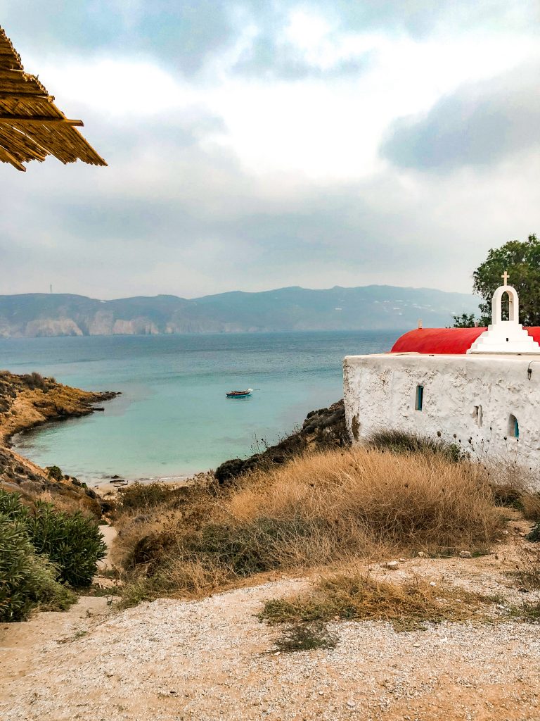 kiki's tavern mykonos, kiki's tavern restaurant agios sostis beach, best restaurants in mykonos, best things to do in mykonos, local cuisine mykonos, view of beach shack looking over agios sostis beach with church with red roof on the beach